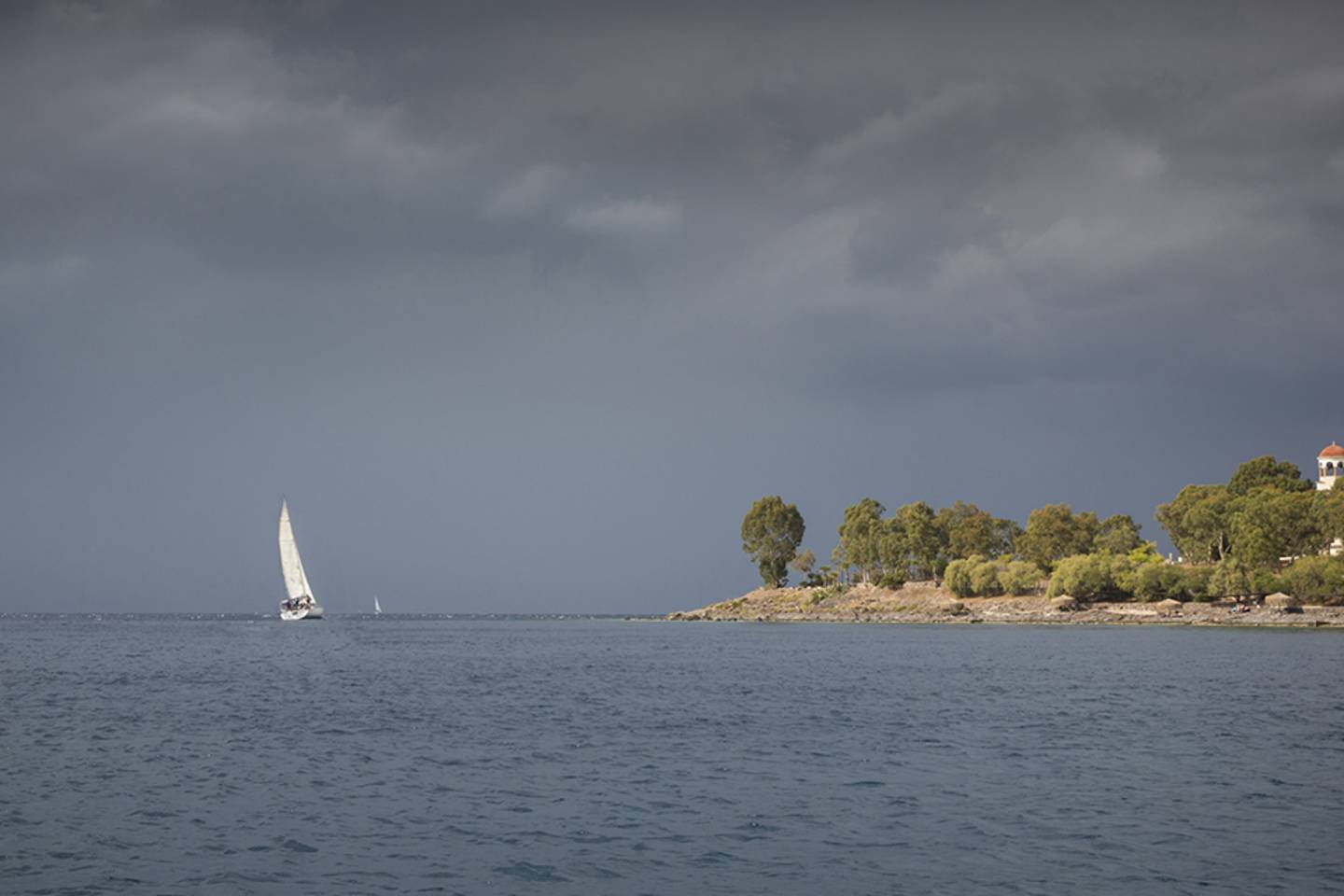 sailboat next to peninsula, grey skies