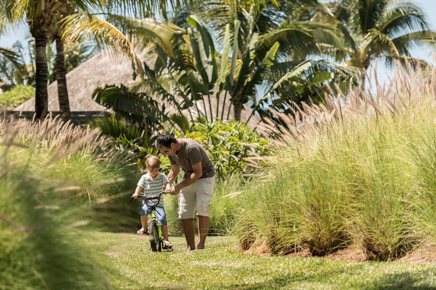 dad helping boy ride bicycle at resort